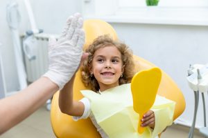 young girl getting a dental checkup and high fiving the dentist