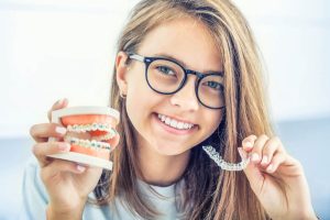young girl with braces in one hand and invisalign in the other