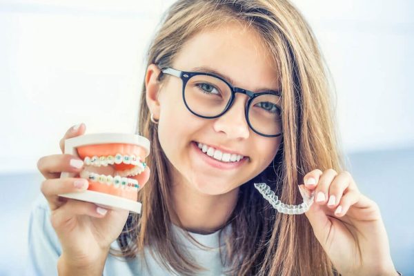 young girl with braces in one hand and invisalign in the other