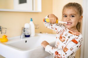 Child brushing teeth at sink, promoting oral hygiene after pediatric tooth extraction, with dental care products visible in the background.