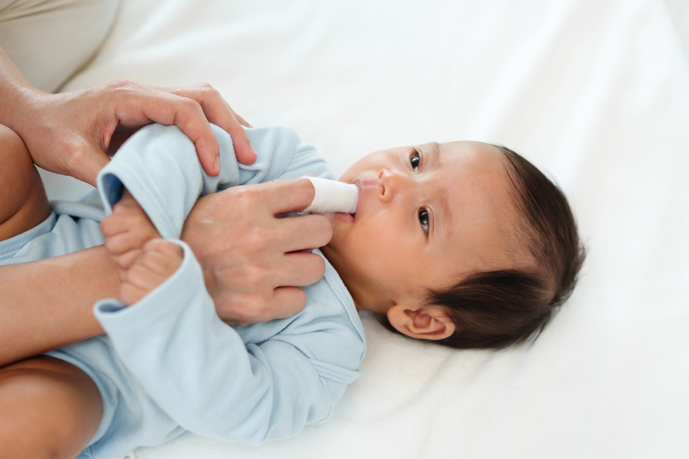 mother using fingers and cloth to clean baby's gums